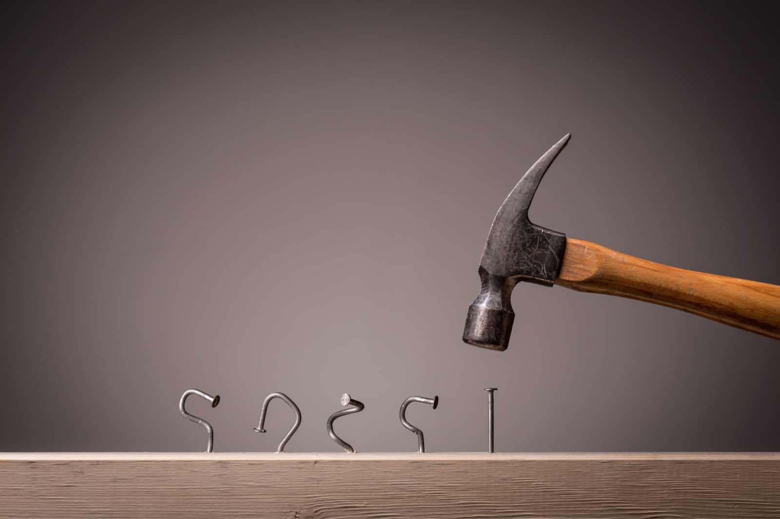 A hammer poised above a wooden surface with various metal hooks and nails arranged in a row